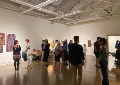Various people looking at artworks on the walls in a dimly lit exhibition hall.