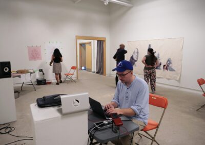 People working at the gallery. The focus is on a man doing something on a laptop, with audio equipment surrounding him.