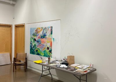 A workspace with a mural in progress hanging on the wall, and various materials on a table.