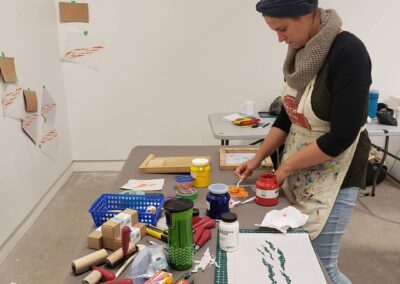 Picture of a woman mixing paint on a table filled with materials.