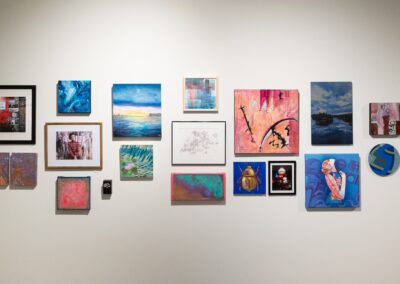 Various artworks from different artists framed on the wall, showcasing paintings, photos and illustrations.