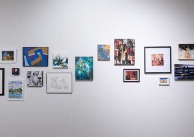 Various artworks from different artists framed on the wall, showcasing drawings, photos and paintings.