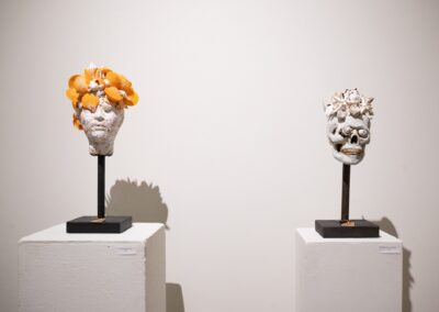 Two sculptures, one of a head and one of a skull. They're both made out of plaster and sea shells, with the shells on the left being bright orange, and the one on the right being white.