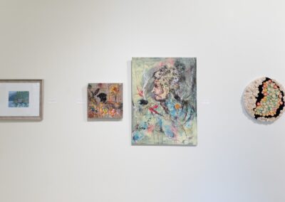 Close-up of one painting on the left, a set of two paintings in the middle and a sculpture on the right. All hanging from the wall.