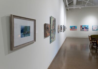 Exhibition hall with various framed paintings from different artists hanging from the walls.